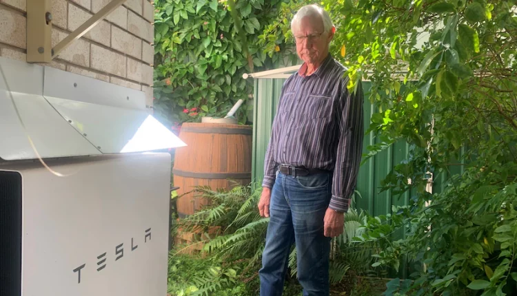 A man stands looking at a Tesla battery on the side of his home.